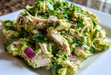 Close-up of creamy avocado chicken salad featuring shredded chicken, diced red onion, and fresh cilantro.