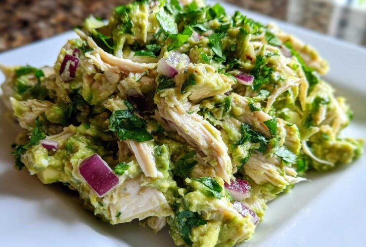 Close-up of creamy avocado chicken salad featuring shredded chicken, diced red onion, and fresh cilantro.