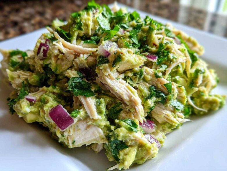 Close-up of creamy avocado chicken salad featuring shredded chicken, diced red onion, and fresh cilantro.