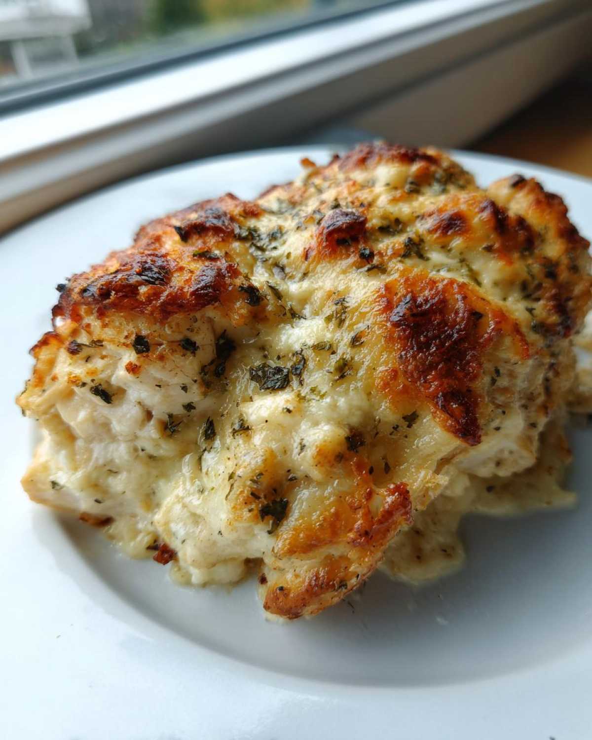 A close-up of a serving of baked caesar chicken topped with melted, browned cheese and herbs.