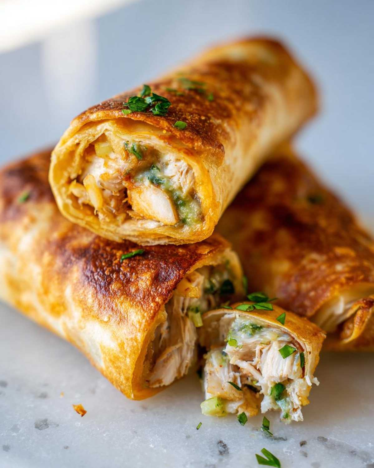 Close-up of crispy baked chicken Chimichangas, one cut open showing shredded chicken filling and green sauce.
