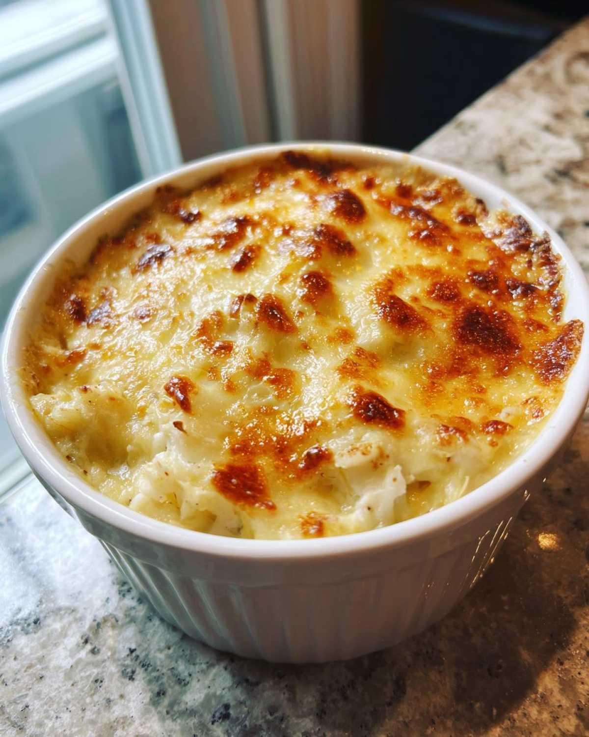 Close-up of creamy, baked hot crab dip with a golden-brown, bubbly cheese topping in a white ramekin.