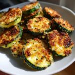 Close-up of golden brown, crispy slices of baked parmesan zucchini piled on a white plate.