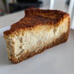 A thick, golden-brown slice of baked Protein Cheesecake with a dense, creamy filling and graham cracker crust.