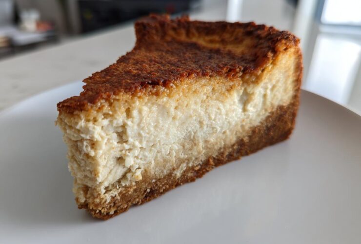 A thick, golden-brown slice of baked Protein Cheesecake with a dense, creamy filling and graham cracker crust.