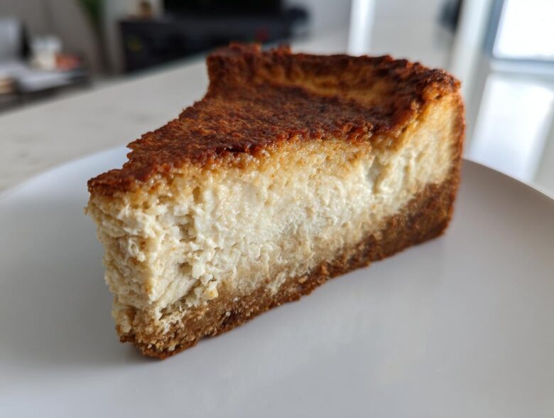 A thick, golden-brown slice of baked Protein Cheesecake with a dense, creamy filling and graham cracker crust.