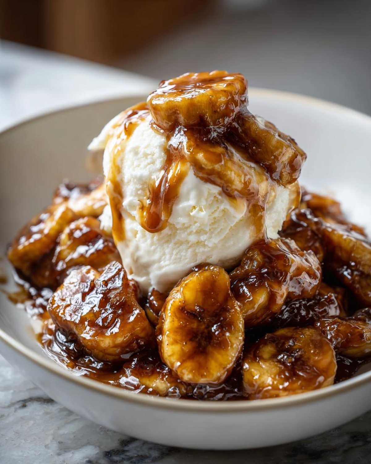 A close-up of rich, caramelized bananas foster served over a scoop of vanilla ice cream in a white bowl.