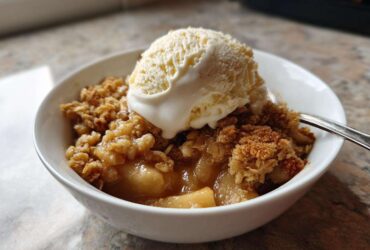 A warm bowl of homemade apple crumble topped with a melting scoop of vanilla ice cream.