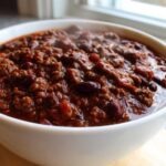 Close-up of a steaming white bowl filled with the best chili recipe, featuring rich ground beef and kidney beans.