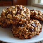 A stack of thick, chewy chocolate chip oatmeal cookie treats piled on a white plate.