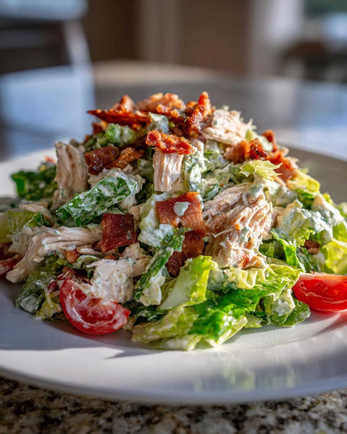 Close-up of a generous serving of blt chicken salad featuring shredded chicken, crisp lettuce, bacon bits, and tomato wedges.