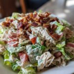 A close-up of a creamy blt chicken salad featuring shredded chicken, lettuce, tomatoes, and crispy bacon pieces.