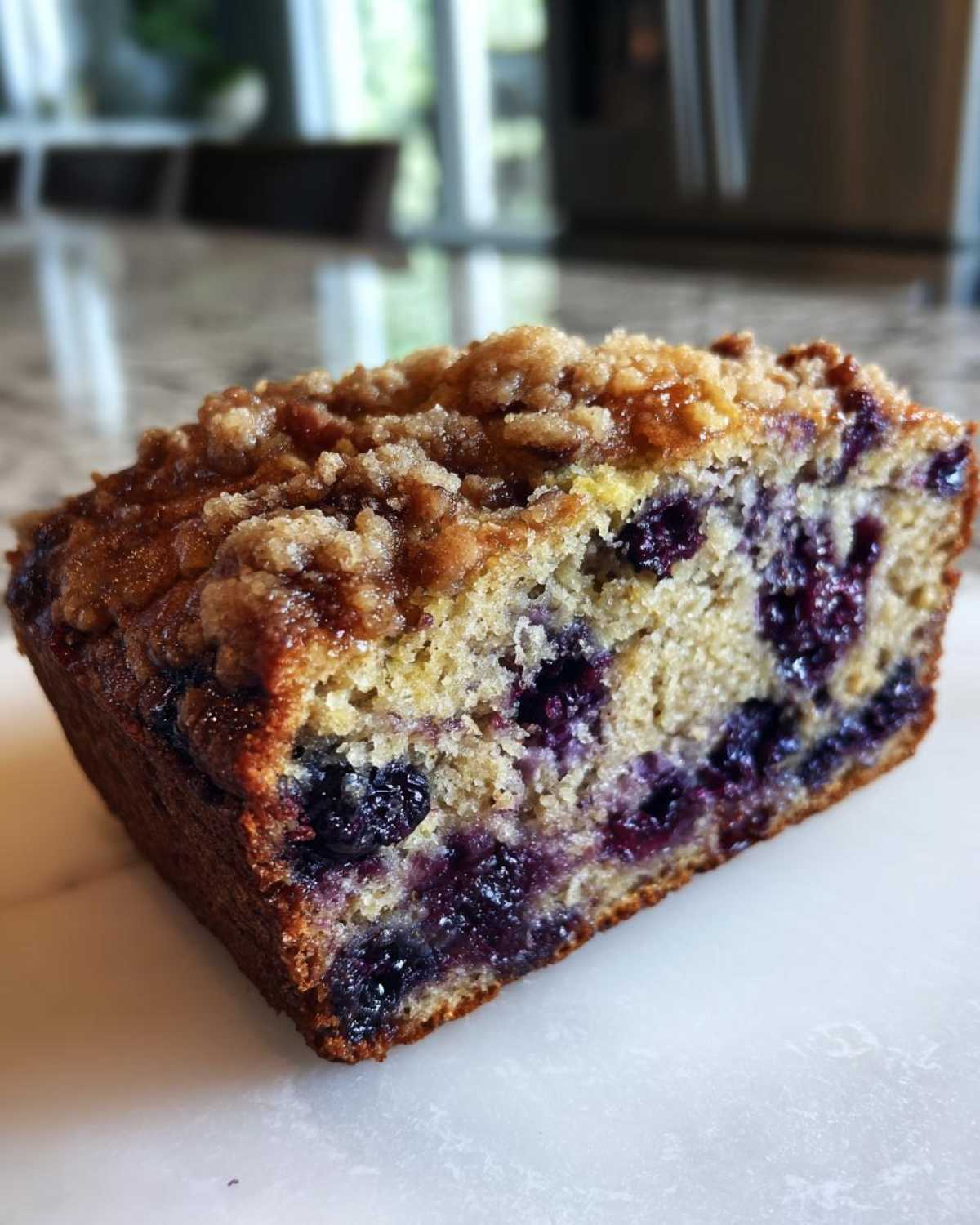 Close-up of a moist slice of blueberry banana bread featuring a crunchy brown sugar streusel topping.