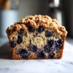 A close-up cross-section of moist blueberry banana bread topped with a thick, golden streusel crumb topping.