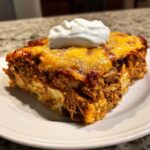 A hearty slice of burrito bake topped with melted cheese and a dollop of sour cream.