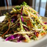 A tall mound of colorful, freshly dressed cabbage salad featuring shredded green and purple cabbage and carrots.