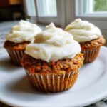 Three delicious carrot cake muffins topped with thick swirls of white cream cheese frosting.