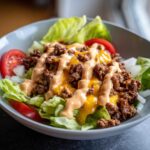 A close-up of a delicious cheeseburger bowl featuring seasoned ground beef, melted cheese, and special sauce over lettuce.