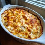 A close-up of a bubbly, baked hot crab dip topped with melted, browned cheese in a white oval baking dish.