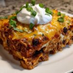 A generous slice of cheesy burrito bake topped with sour cream and green onions on a white plate.