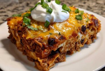A generous slice of cheesy burrito bake topped with sour cream and green onions on a white plate.