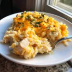 A serving of creamy cheesy chicken and rice topped with melted cheddar and parsley, being lifted by a fork.