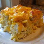 A close-up serving of cheesy chicken and rice casserole topped with melted, browned cheddar cheese.