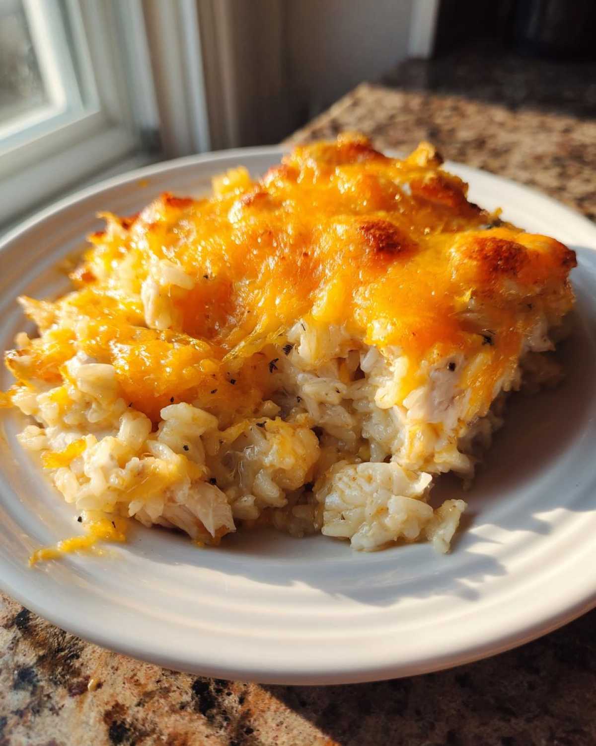 A scoop of creamy cheesy chicken and rice casserole topped with melted, browned cheddar cheese.