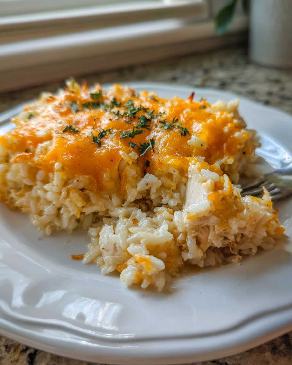 A serving of cheesy chicken and rice casserole topped with melted cheddar and parsley on a white plate.