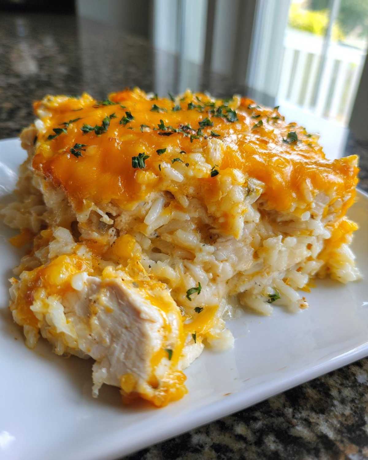 A close-up serving of cheesy chicken and rice casserole topped with melted cheddar and parsley.