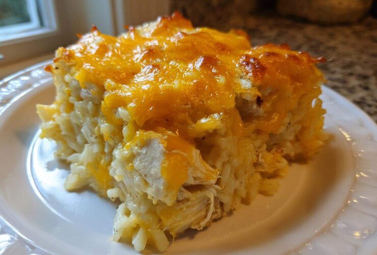 A close-up serving of cheesy chicken and rice casserole topped with melted, browned cheddar cheese.