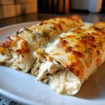 Close-up of two cheesy chicken enchiladas with melted white cheese and green sauce spilling over shredded chicken.