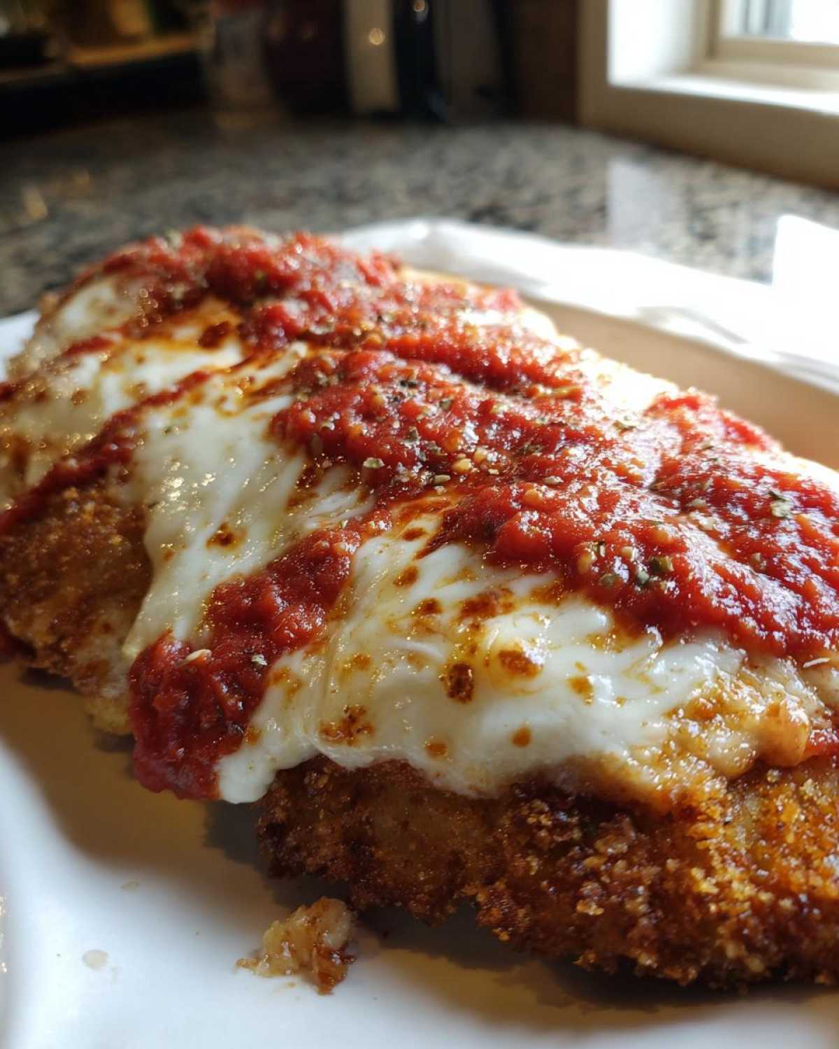 A close-up of a breaded chicken parmesan recipe piece topped with melted mozzarella and marinara sauce.