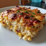 A close-up of a baked square serving of creamy street corn dip, topped with a golden-brown, bubbly cheese crust and parsley.