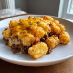 A close-up serving of tater tot casserole featuring crispy tots, ground beef, and melted cheddar cheese.