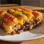 A close-up serving of tater tot casserole showing crispy tater tots, melted cheddar cheese, and a ground beef layer.