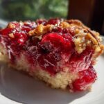 Close-up of a moist slice of cherry dump cake showing bright red cherry filling and crumbly topping on a white plate.