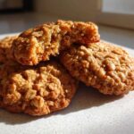 Close-up of several chewy oatmeal cookies, one broken open to show the texture.