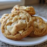 Close-up of chewy white chocolate macadamia nut cookies stacked on a white plate.