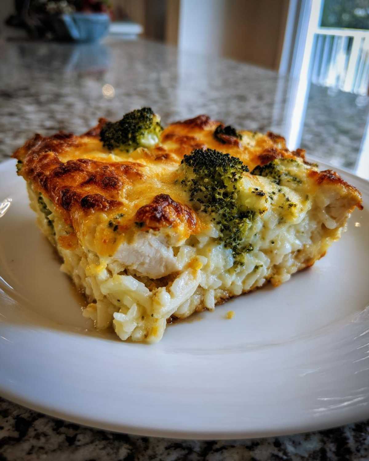 A close-up serving of cheesy chicken broccoli rice casserole with a golden-brown top.