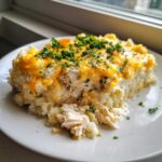 A hearty serving of chicken cauliflower rice casserole topped with melted cheddar cheese and fresh parsley.