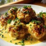Close-up of browned chicken piccata meatballs covered in a creamy lemon-caper sauce and fresh parsley.