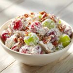 A creamy bowl of chicken salad chick grape salad mixed with red and green grapes and topped with pecans.