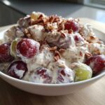 A white bowl filled with creamy chicken salad chick grape salad, topped with chopped pecans.