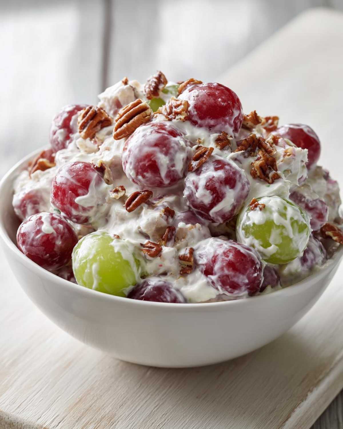 A white bowl filled with creamy chicken salad chick grape salad, featuring red and green grapes and chopped pecans.