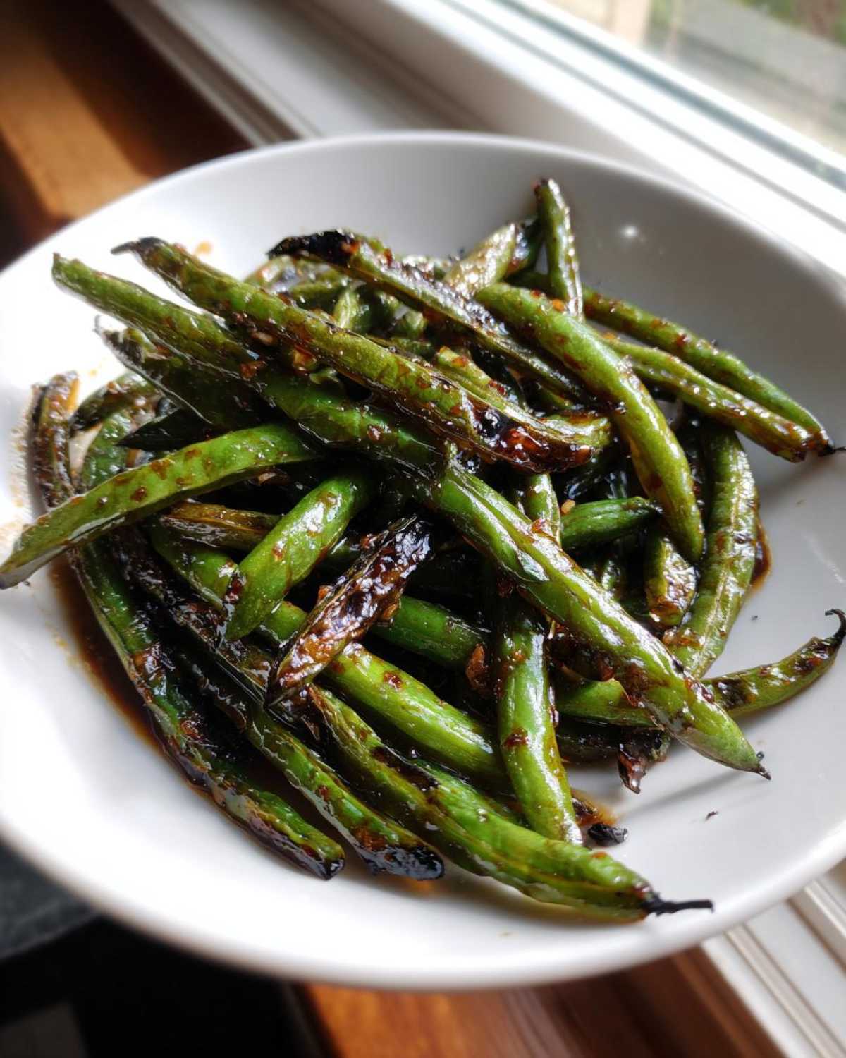 A close-up of blistered chinese green beans with garlic sauce served in a white bowl.