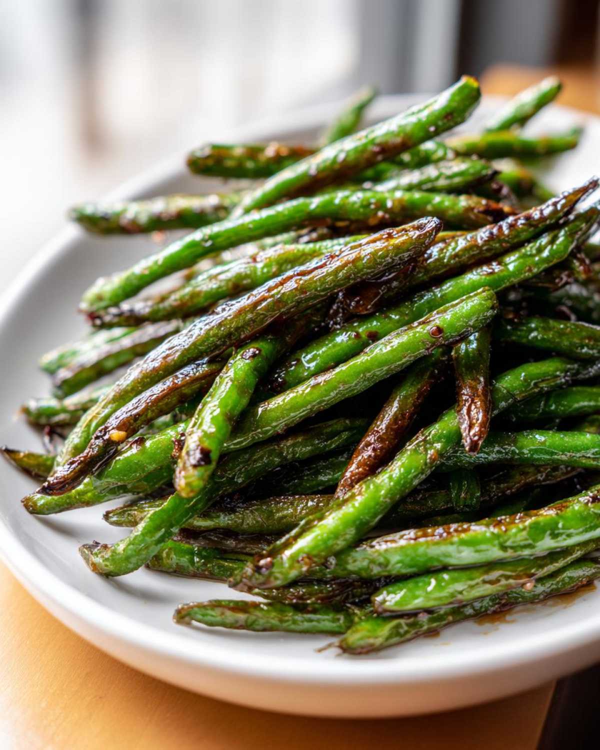 A close-up of vibrant, blistered chinese green beans with garlic sauce piled high on a white plate.