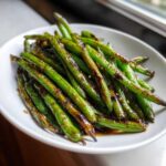 A white bowl filled with vibrant, blistered chinese green beans with garlic sauce, showing a glossy dark glaze.