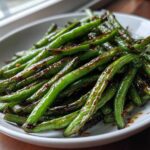 A close-up of glossy, blistered chinese green beans with garlic sauce served in a white bowl.
