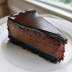 A decadent slice of rich chocolate cheesecake with a dark chocolate crust and glossy ganache topping.